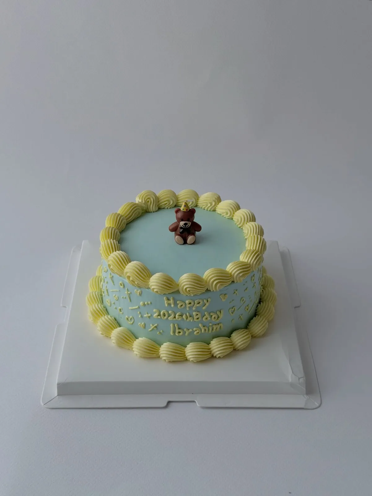 Blue cake with teddy bear topper and cream shell border, bespoke celebration cake from Danine Cakes, South London