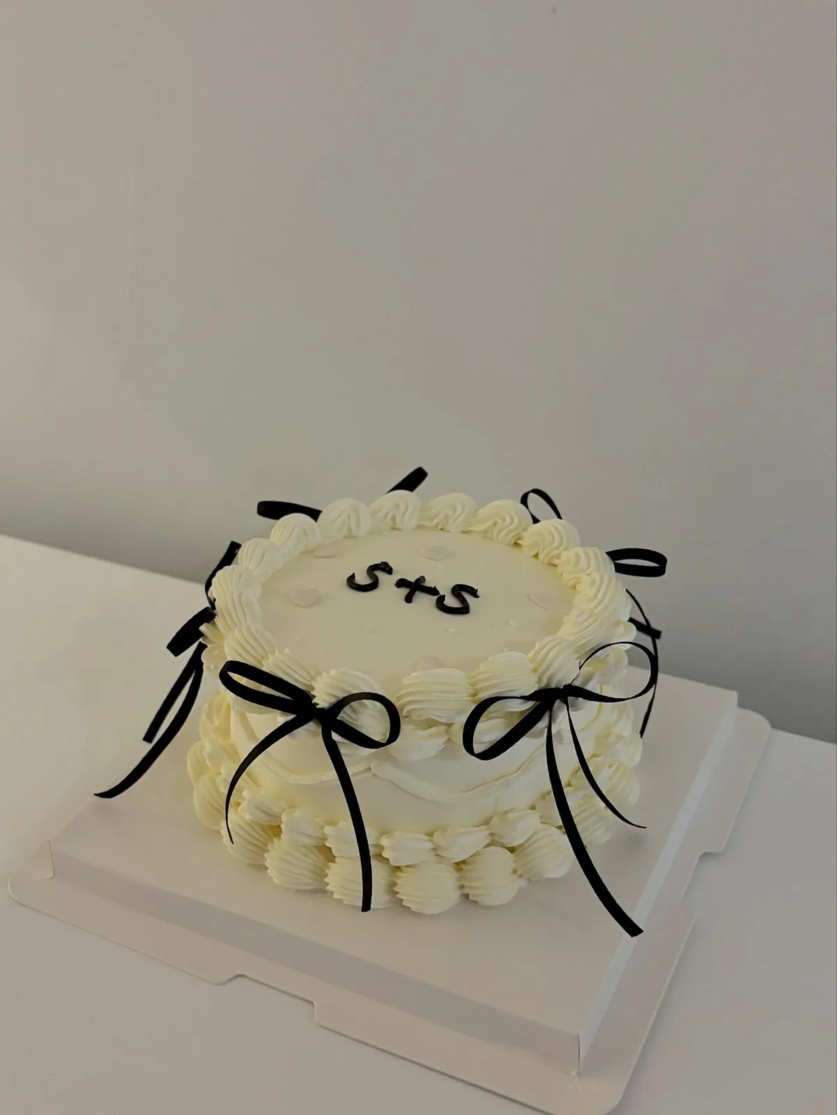 Cream cake with black bows and piped initials, Korean-inspired custom cake handmade in Streatham, London