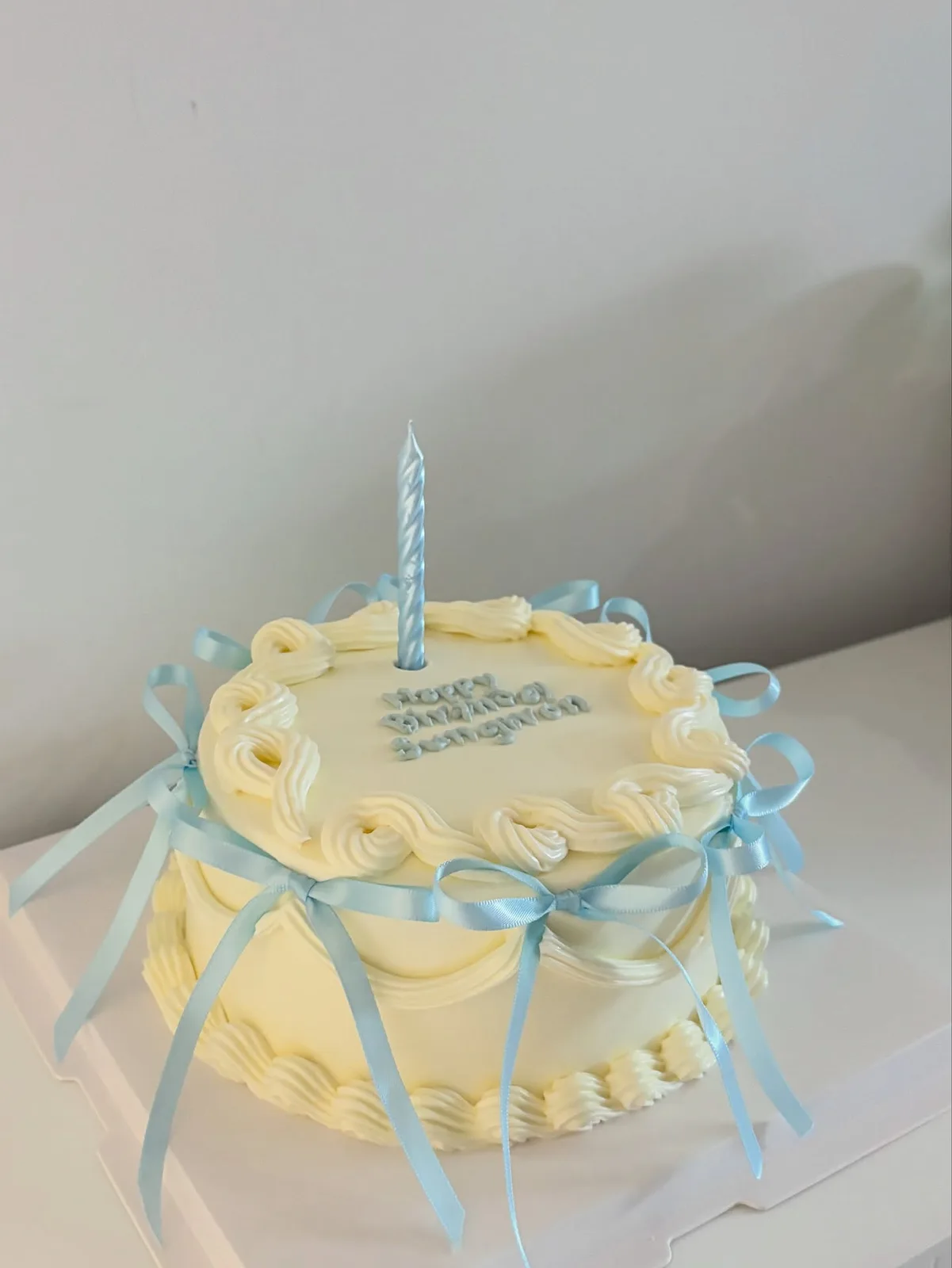 Cream cake with blue bows and birthday candles, handmade to order by Danine Cakes in Streatham, South London