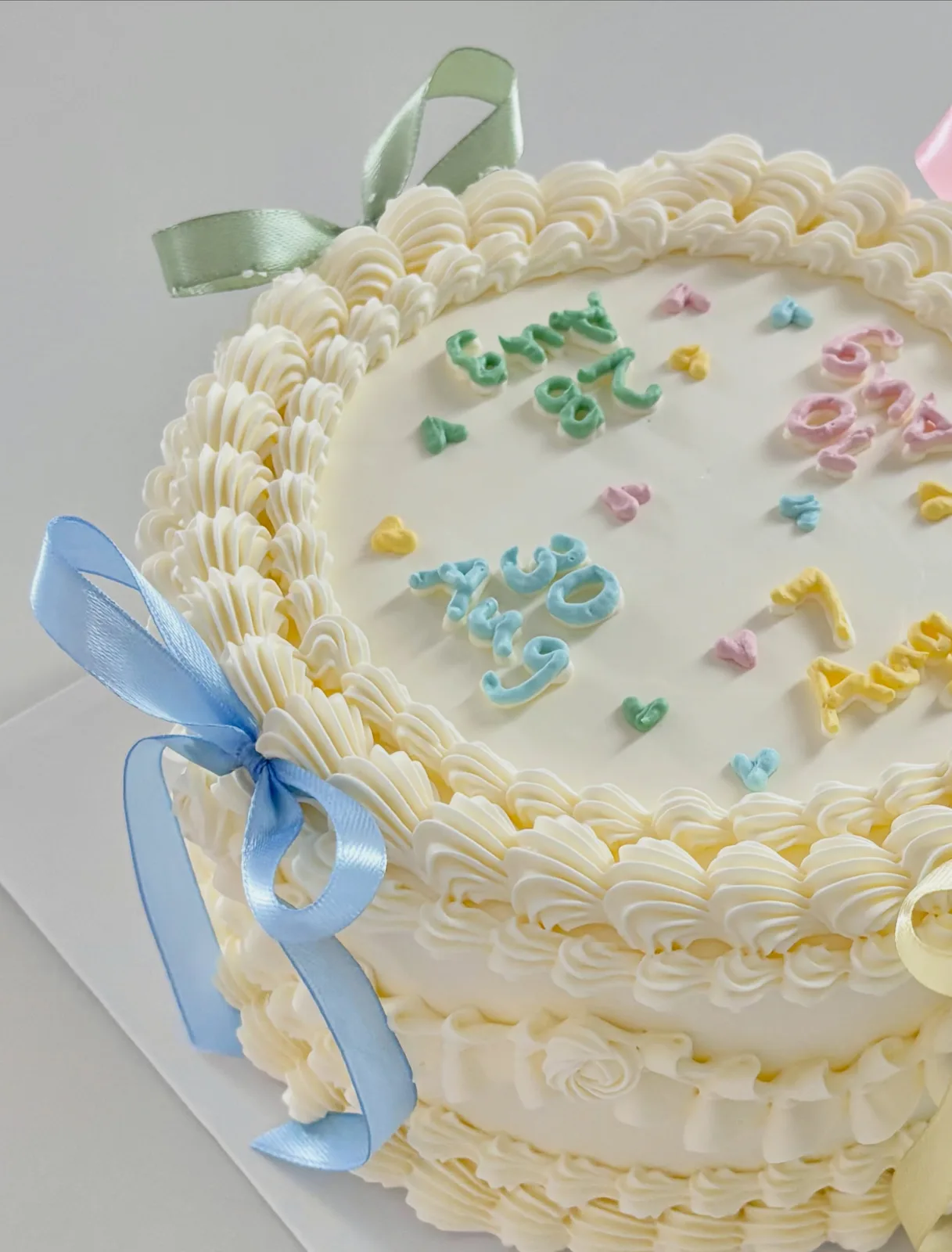 Cream cake with pastel piping and blue ribbon, bespoke celebration cake from Danine Cakes, South London