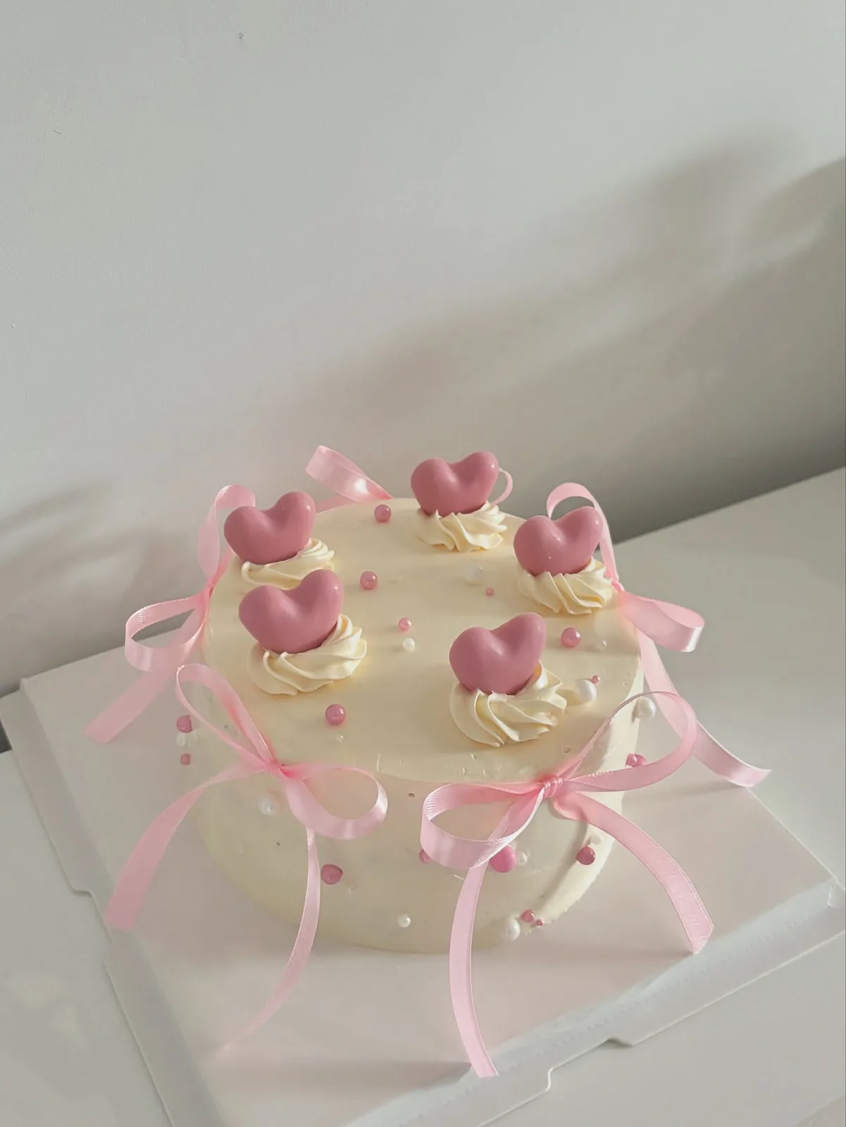 Cream cake with pink hearts and satin ribbons, handmade to order by Danine Cakes in Streatham, South London