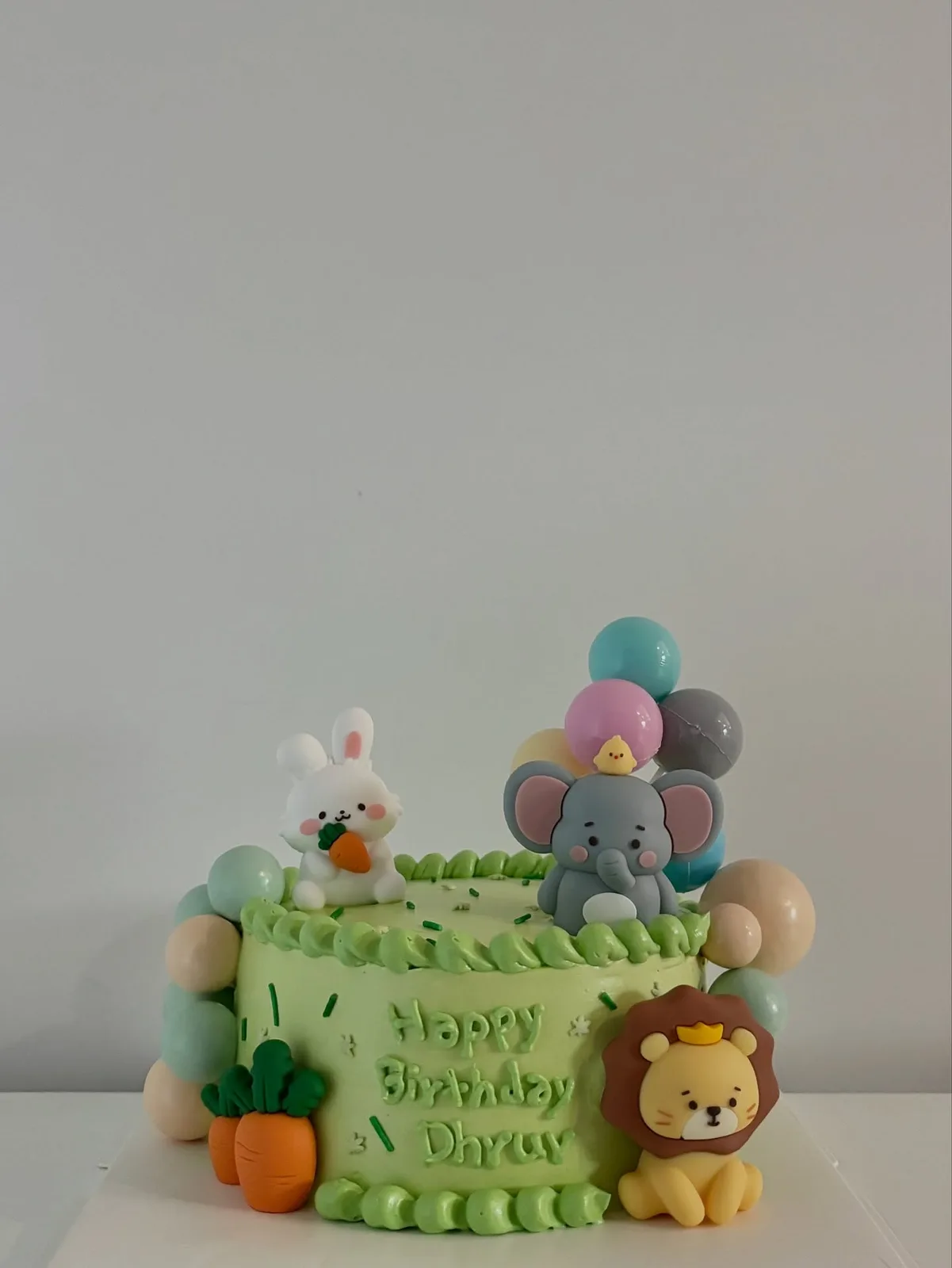 Green cake with elephant, rabbit and balloon toppers, bespoke celebration cake from Danine Cakes, South London
