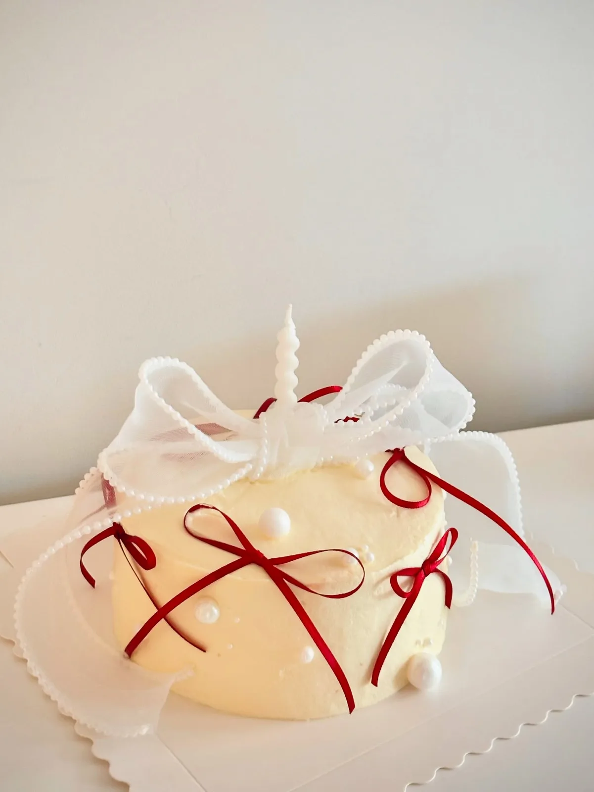 Ivory piped dome cake with red ribbons and bow, handmade to order by Danine Cakes in Streatham, South London