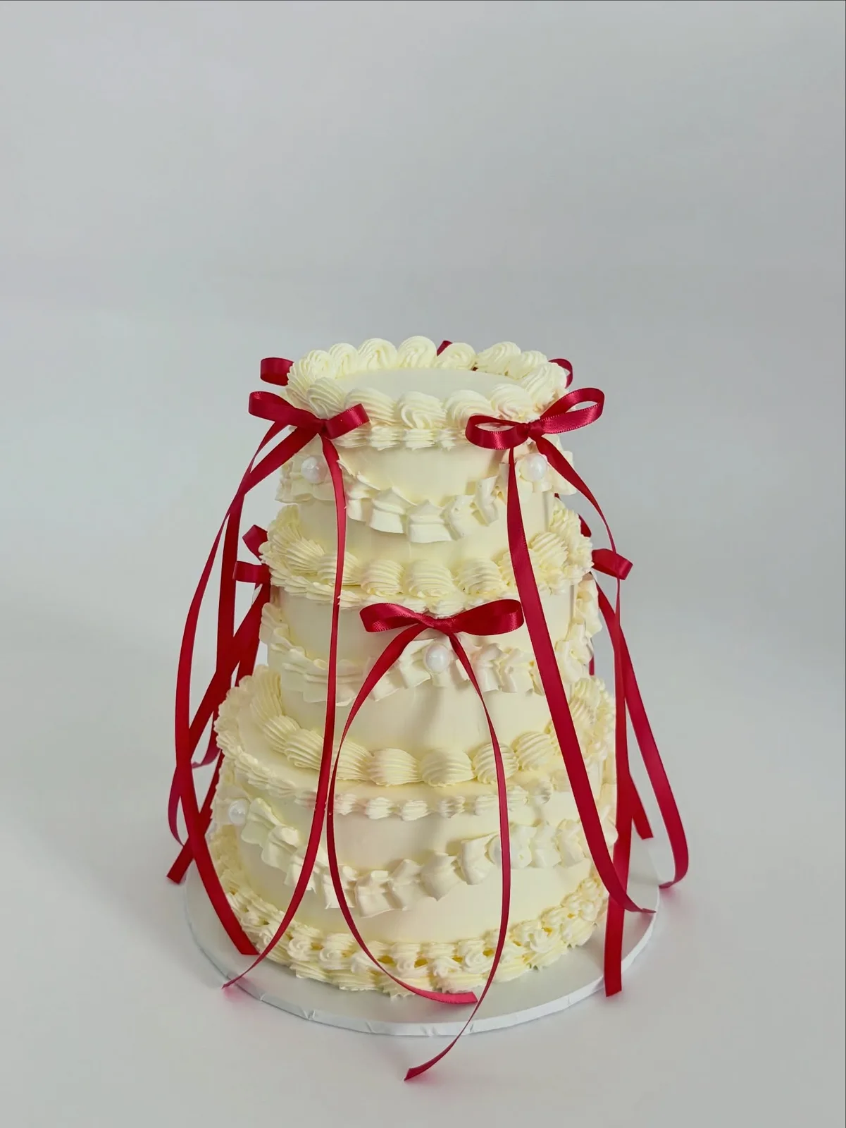 Ivory piped dome cake with red ribbons and pearls, bespoke celebration cake from Danine Cakes, South London
