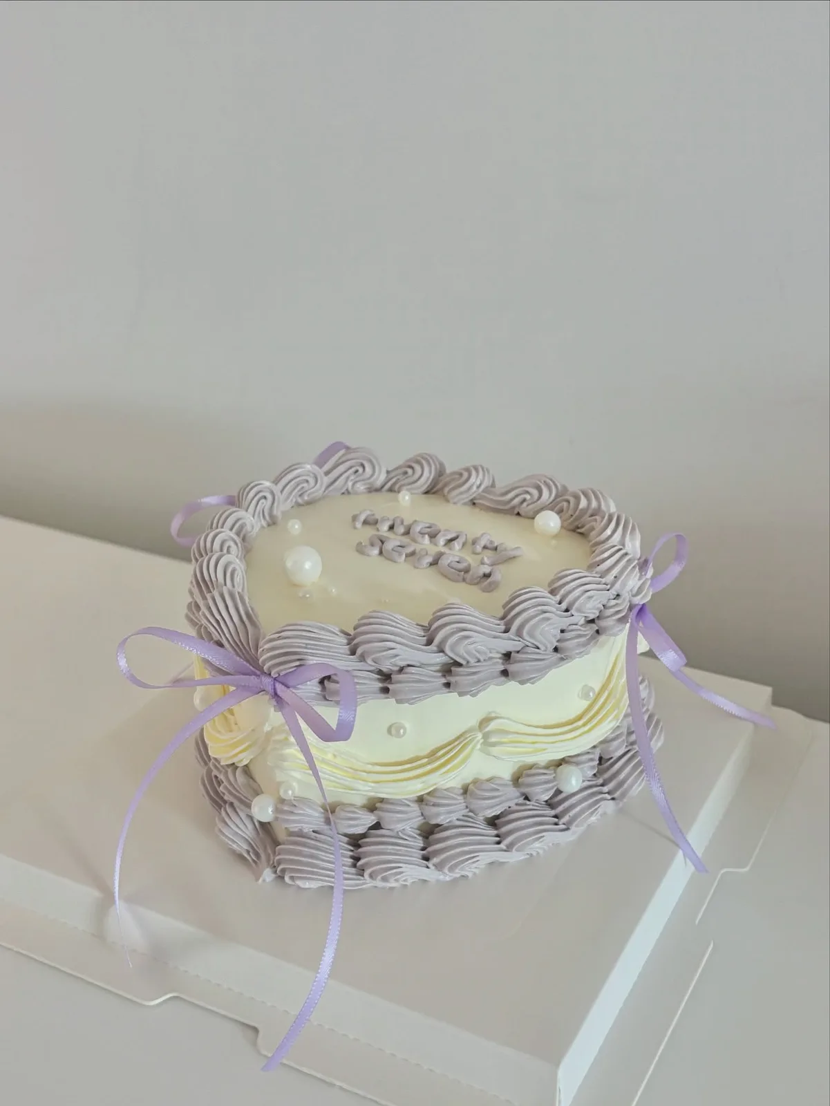Lilac and cream cake with piped scrolls and ribbons, handmade to order by Danine Cakes in Streatham, South London