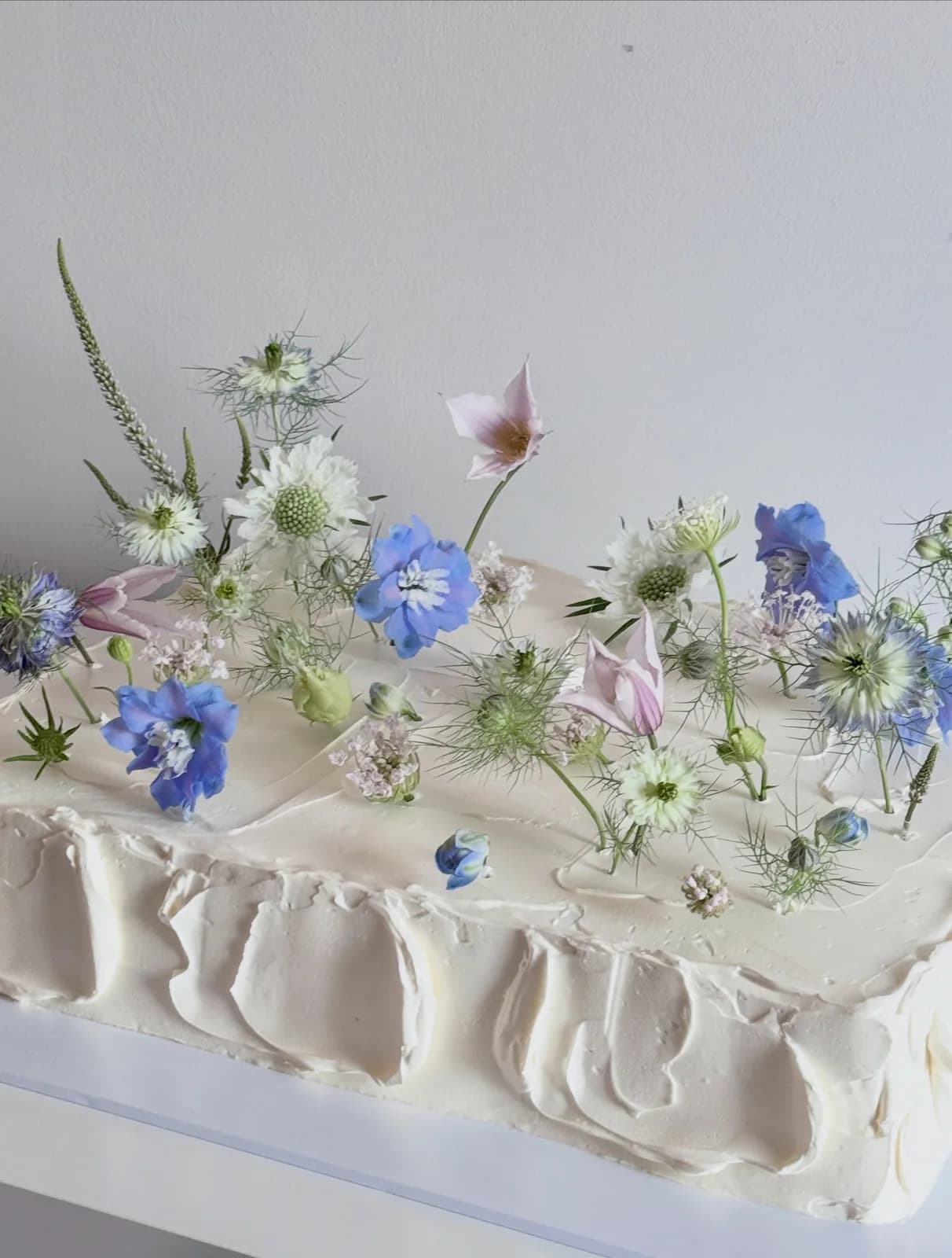 Long white cake with fresh blue and white flowers, handmade to order by Danine Cakes in Streatham, South London