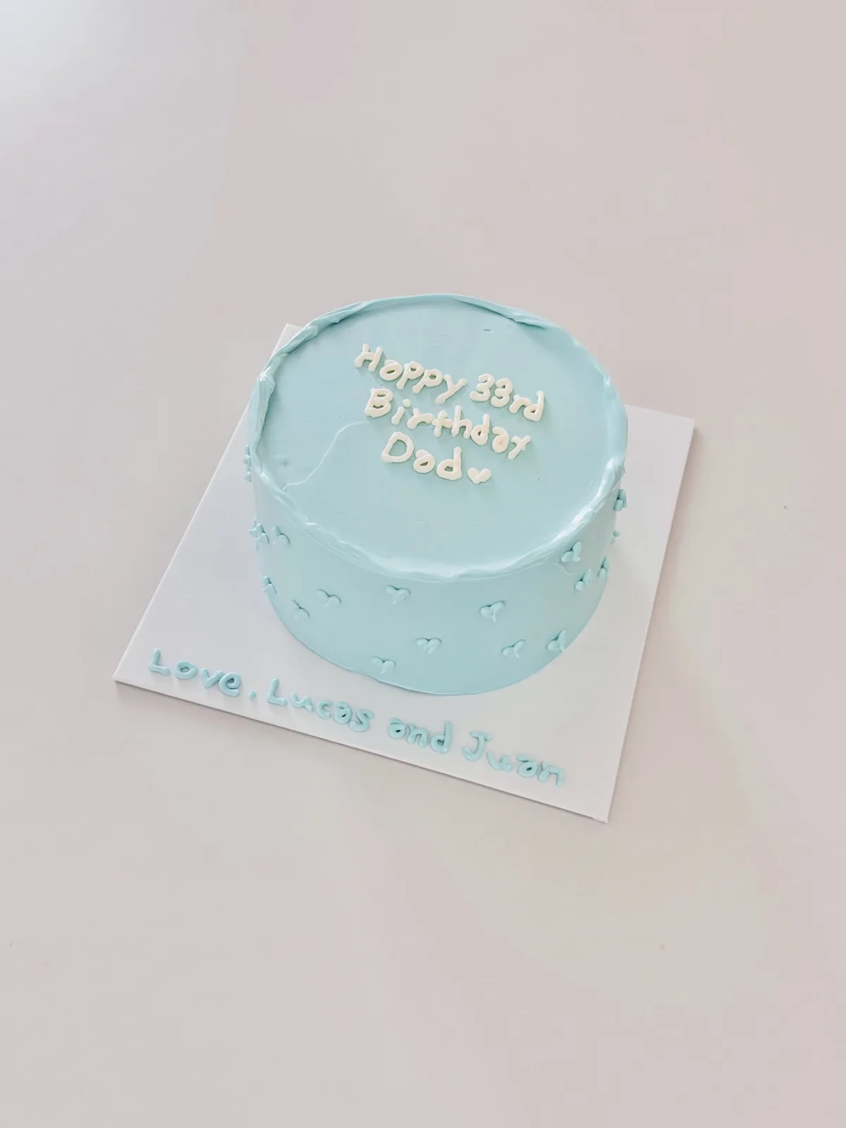 Pale blue cake with white dots and piped lettering, bespoke celebration cake from Danine Cakes, South London