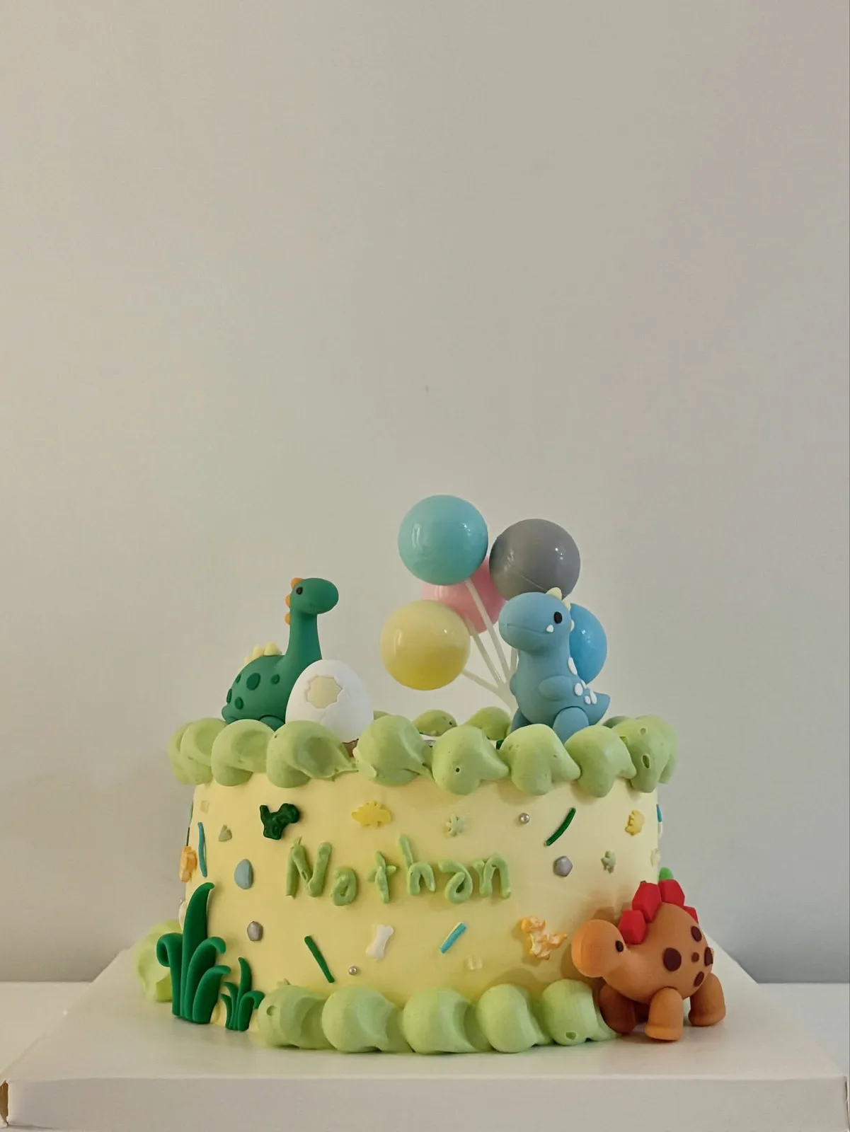 Pale yellow cake with dinosaur and balloon toppers, handmade to order by Danine Cakes in Streatham, South London