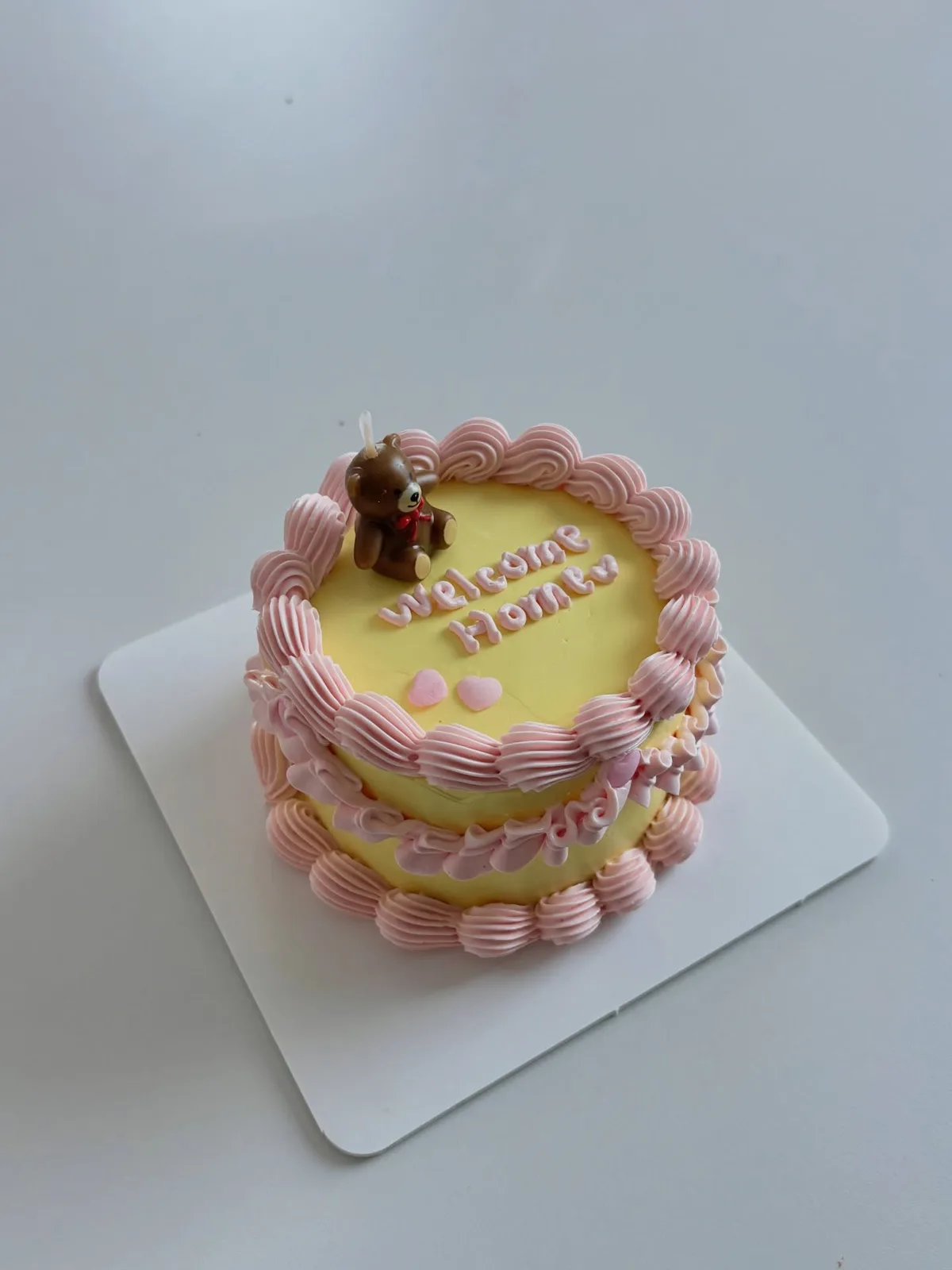 Pale yellow cake with pink shell border and teddy bear topper, handmade to order by Danine Cakes in Streatham, South London