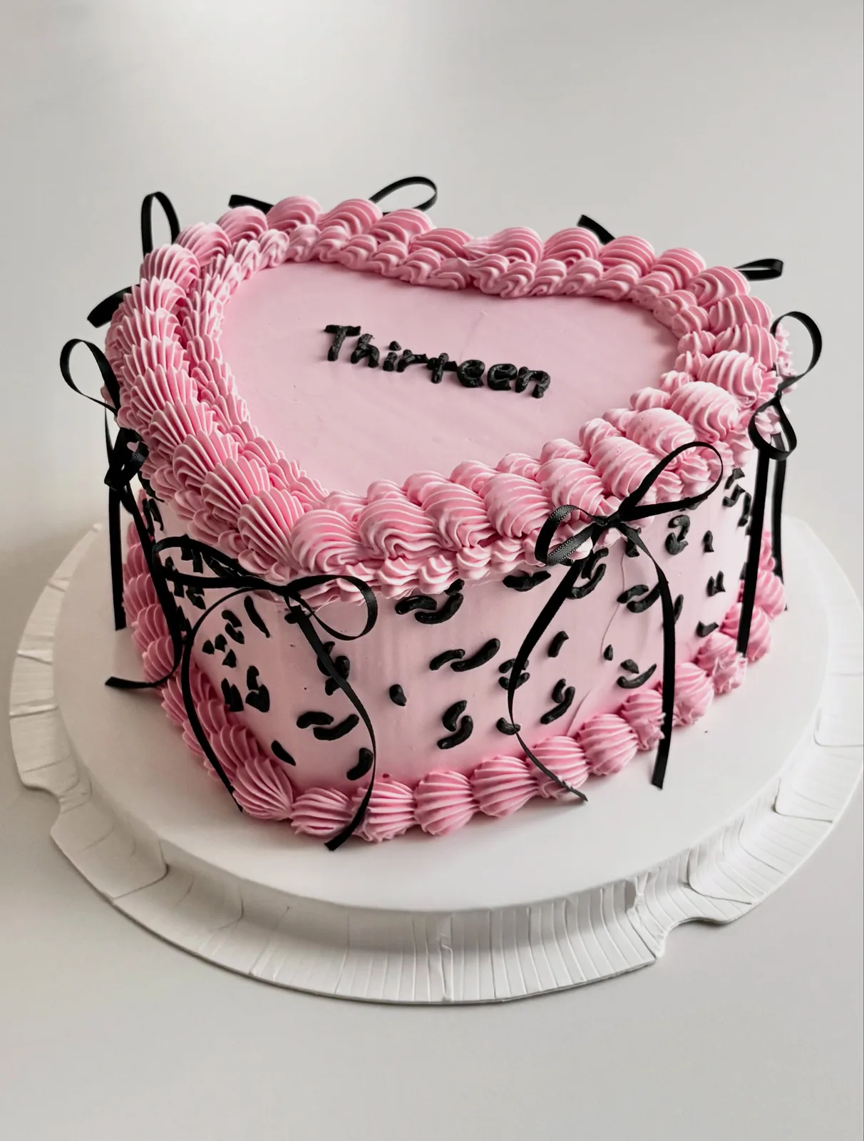 Pink heart cake with black bows and piped shell border, bespoke celebration cake from Danine Cakes, South London