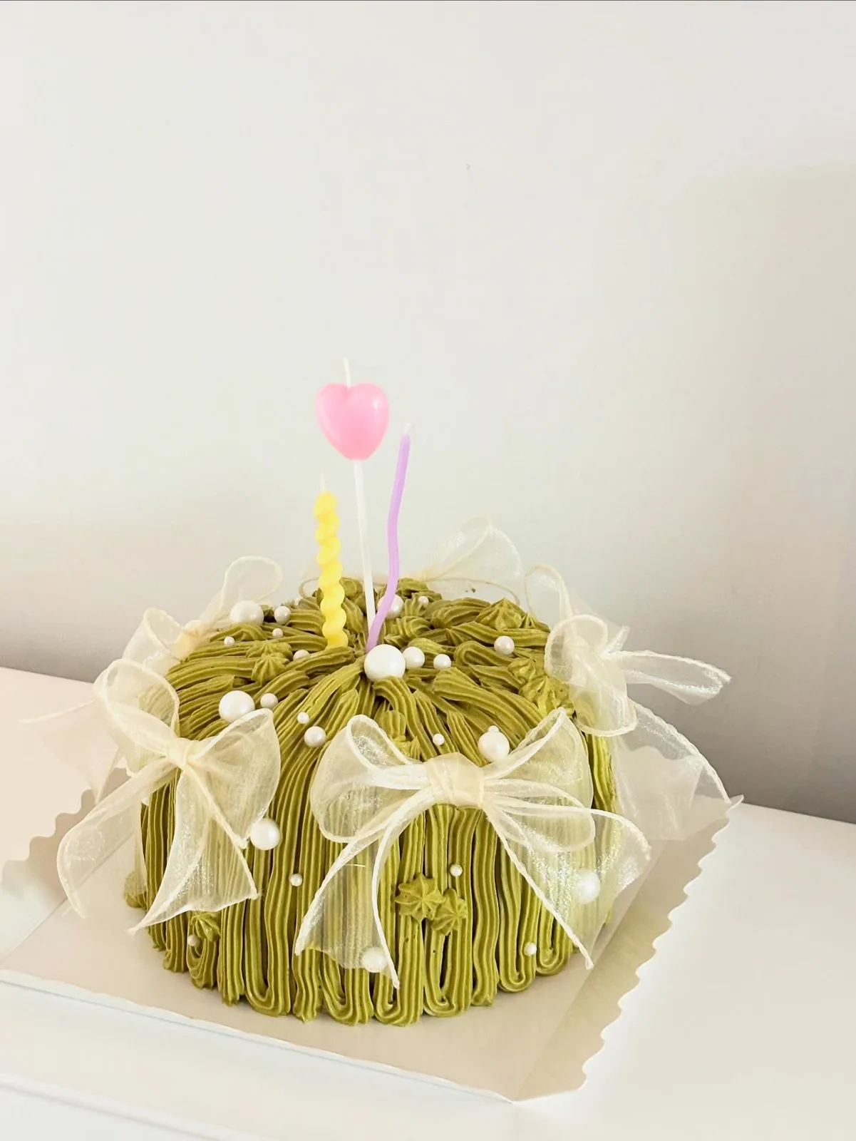 Pistachio piped strand cake with white bow and tulip candle, handmade to order by Danine Cakes in Streatham, South London