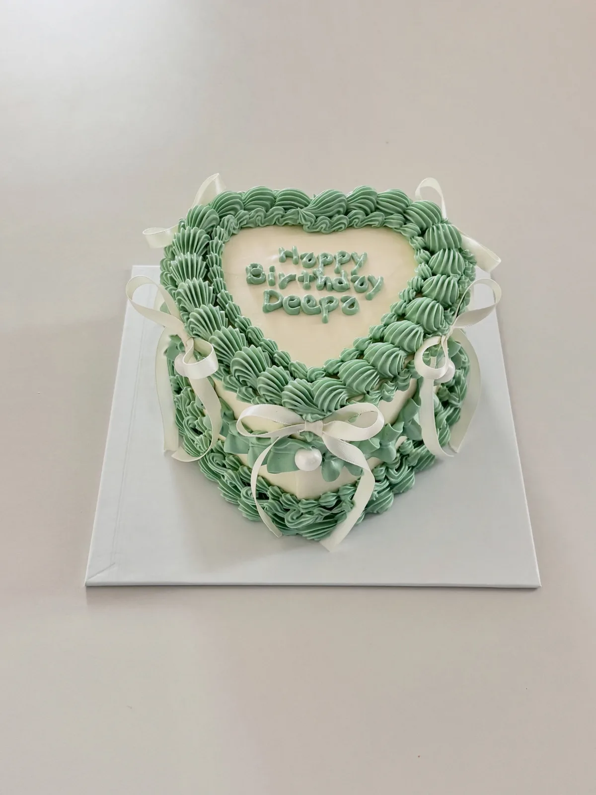 Sage green heart cake with white bows and piping, Korean-inspired custom cake handmade in Streatham, London
