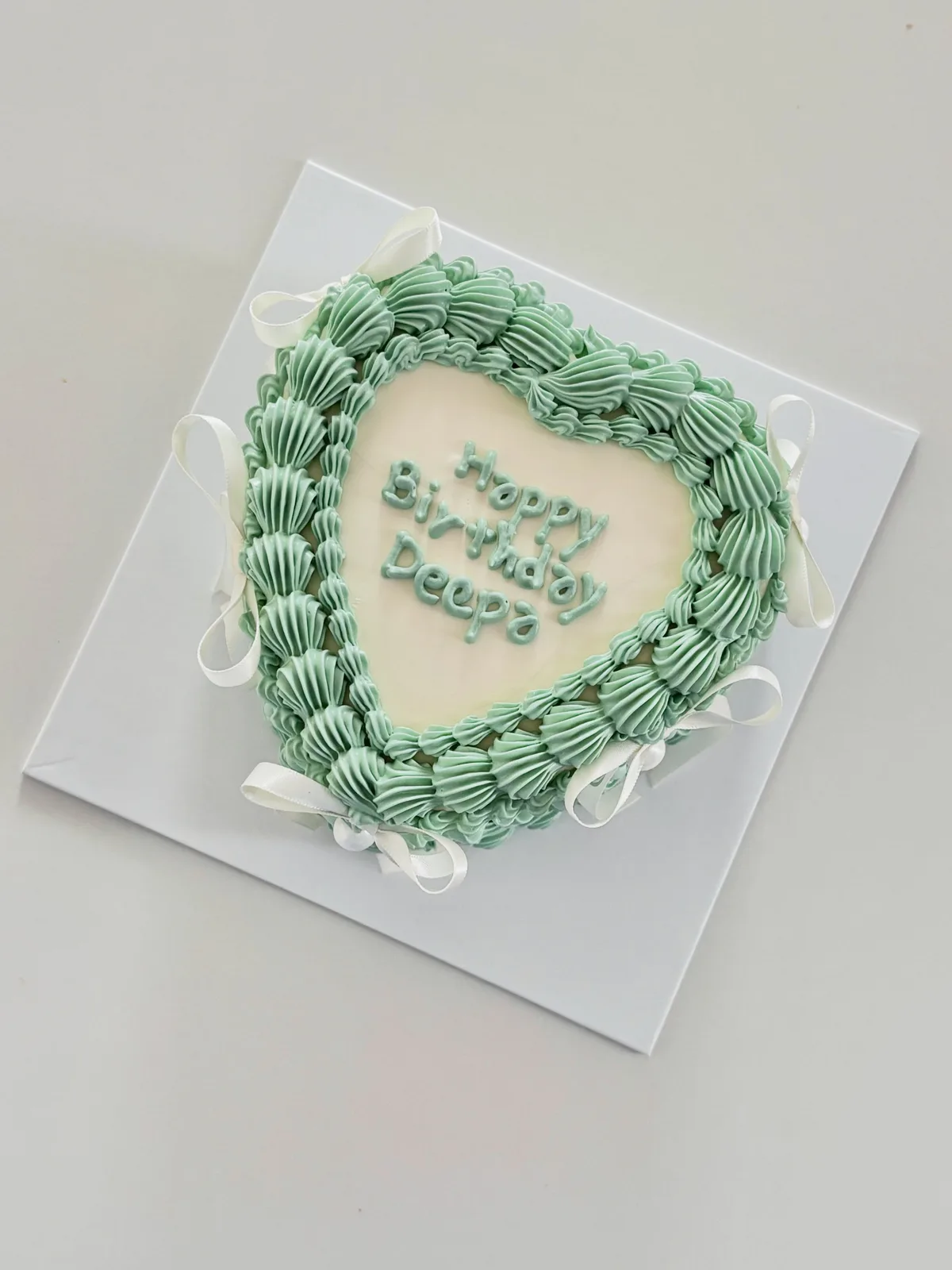 Sage green heart cake with white bows and piping, Korean-inspired custom cake handmade in Streatham, London