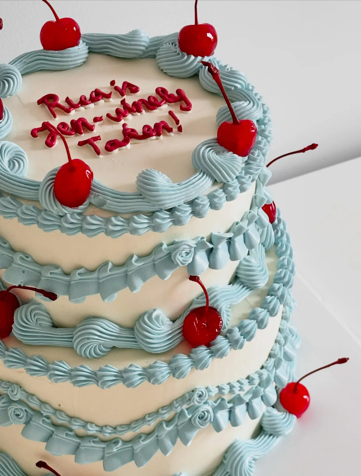 Three tier blue cake with cherries and piped scrolls, handmade to order by Danine Cakes in Streatham, South London