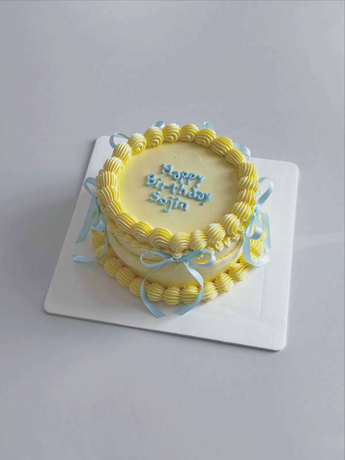 Yellow cake with piped border and blue ribbons, handmade to order by Danine Cakes in Streatham, South London