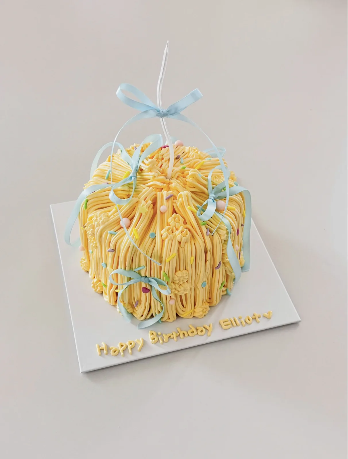 Yellow piped strand cake with blue ribbon bow, custom cake made in Streatham SW16 - Danine Cakes