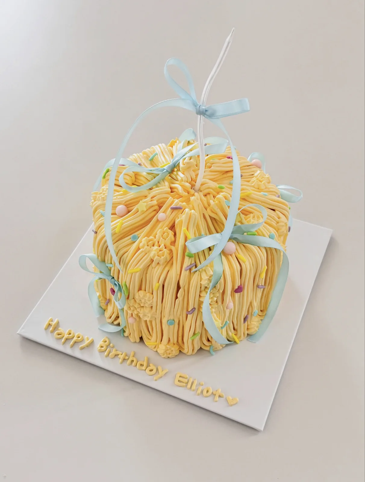 Yellow piped strand cake with blue ribbon bow, handmade to order by Danine Cakes in Streatham, South London