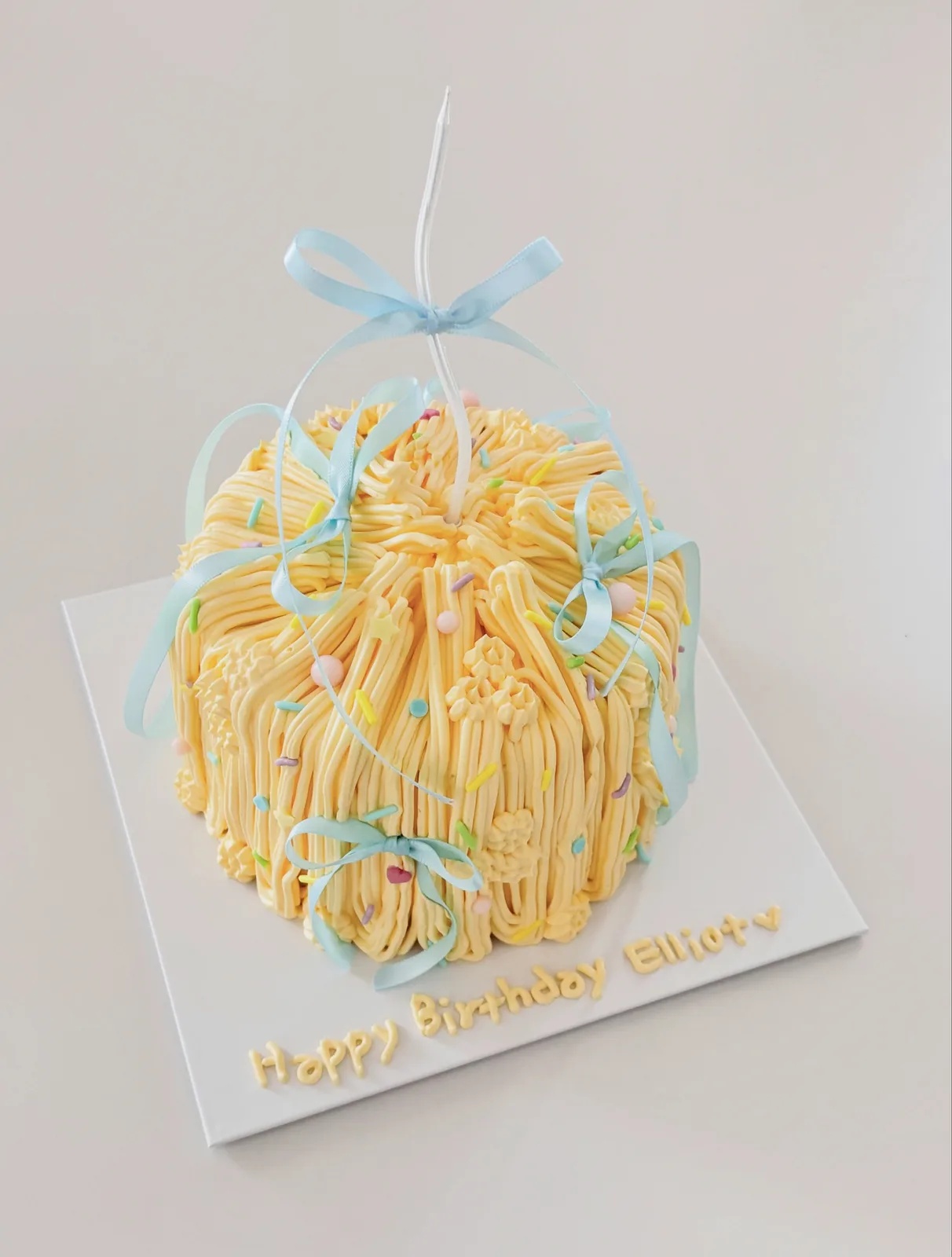 Yellow piped strand cake with blue ribbon bow, handmade to order by Danine Cakes in Streatham, South London