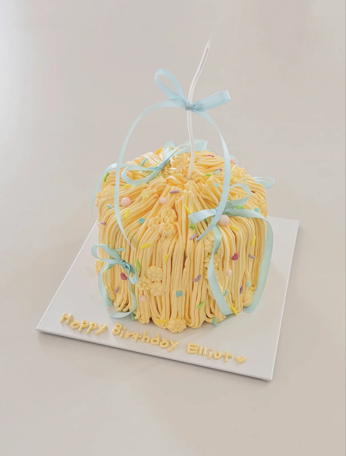 Yellow piped strand cake with blue ribbon bows, bespoke celebration cake from Danine Cakes, South London
