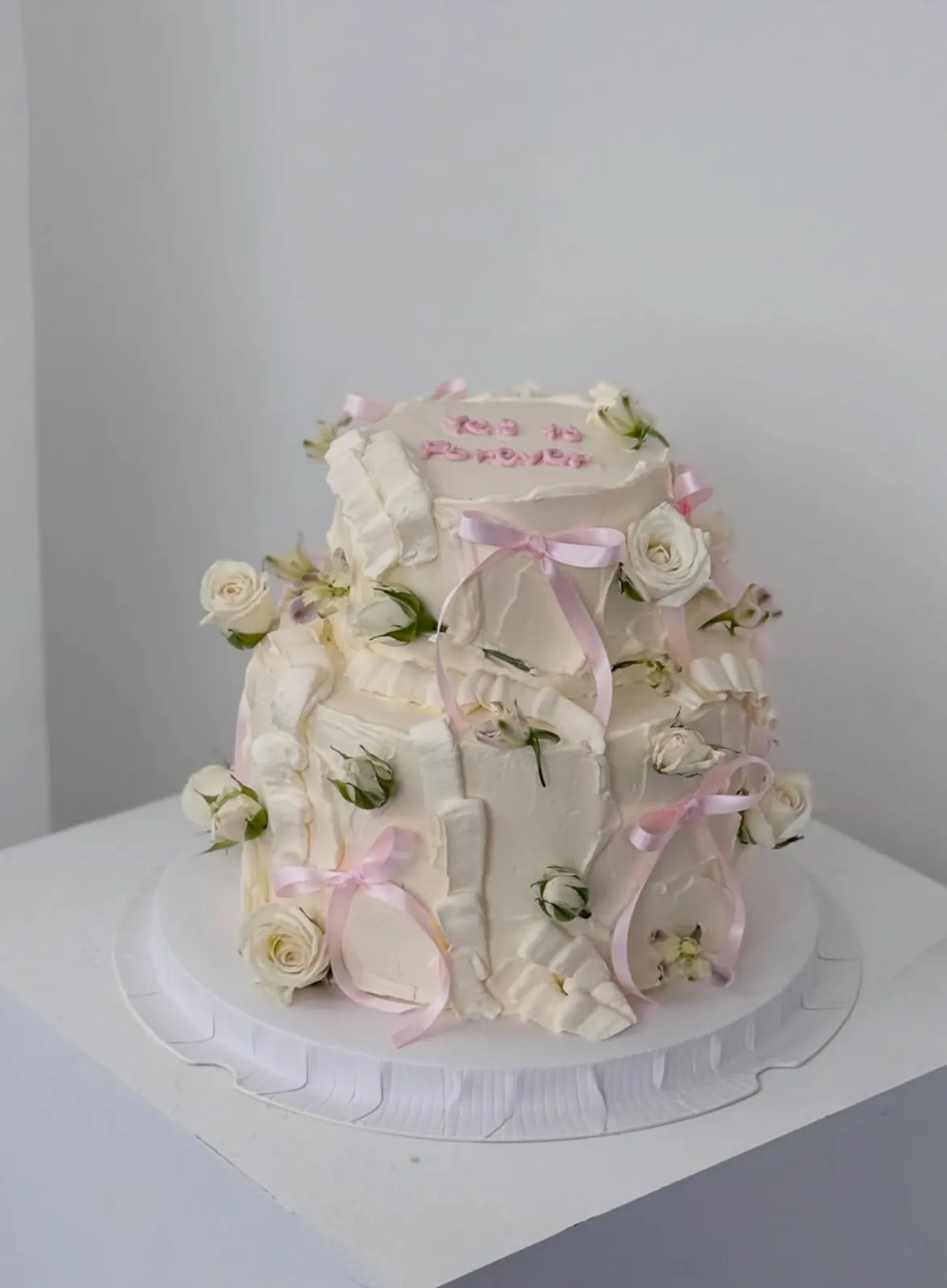 Two-tier white buttercream cake with fresh white roses and pink ribbon bows